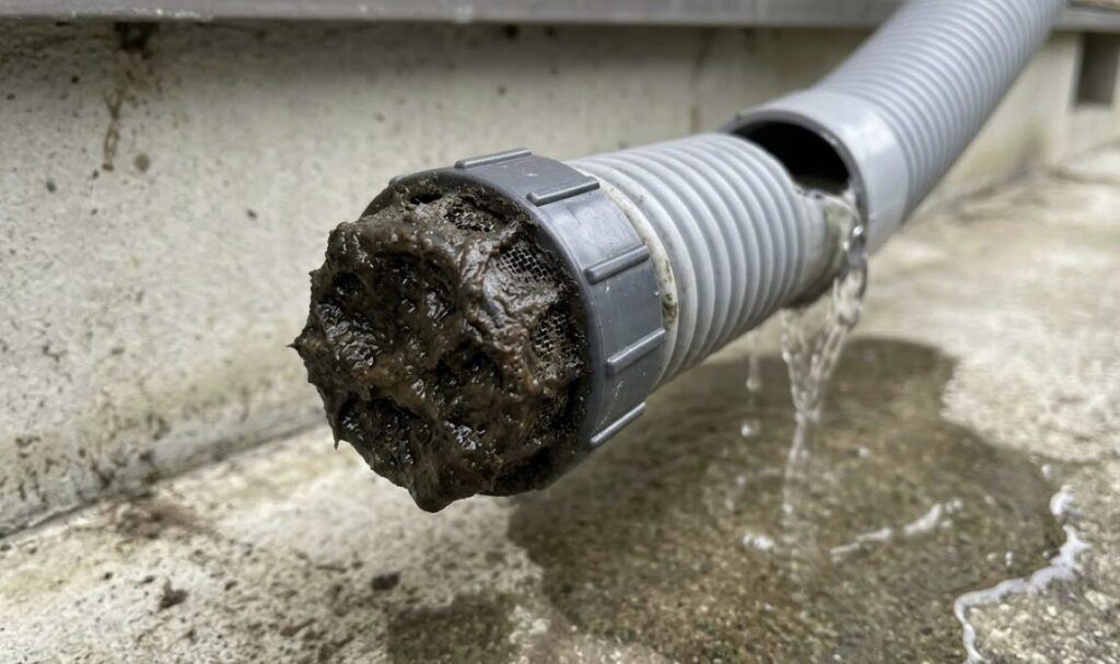 エアコンのドレンホース先端に取り付けられ、ホコリとカビのヘドロで完全に目詰まりした防虫キャップ