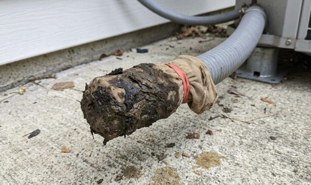 エアコンのドレンホース先端にストッキングが被せられ、汚れで完全に泥だんごのように目詰まりした状態