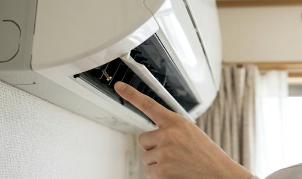 エアコンの外装カバーを外す際、吹き出し口付近の化粧カバーの奥に隠されたネジを指差す日本人男性。