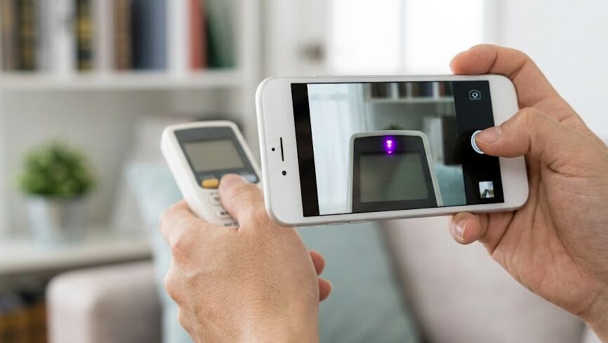 スマートフォンのカメラ越しにエアコンリモコンの送信部を確認する様子。スマホ画面上で先端のランプが光っているかを判別。