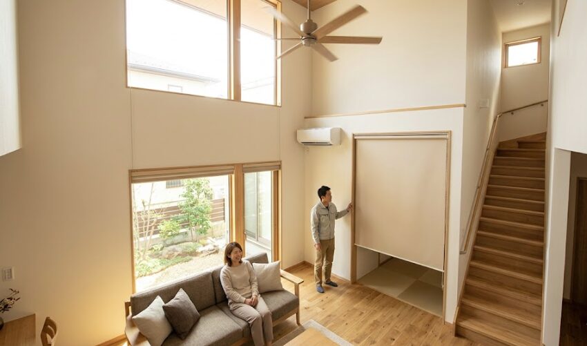 吹き抜けのあるリビングで、シーリングファンが回り、リビング階段の入り口にロールスクリーンを設置して暖気の流出を防いでいる様子。