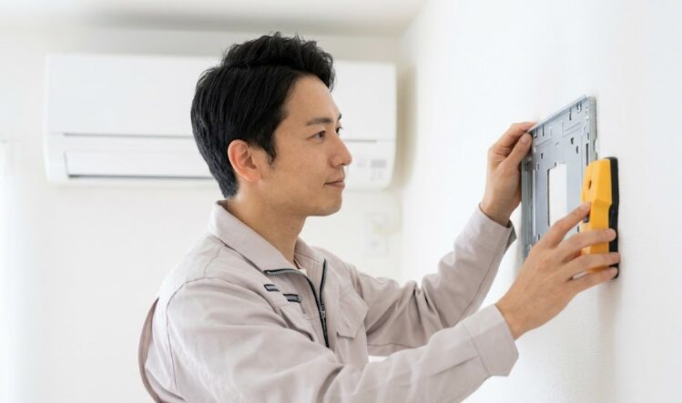 エアコン設置を検討する工務店のプロが石膏ボードの壁と下地を確認している様子。信頼と安全の象徴。