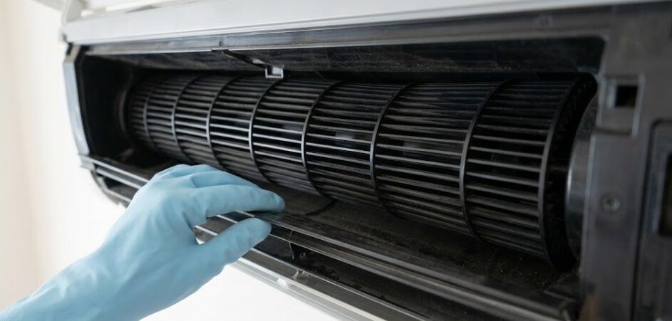 日本の家庭用壁掛けエアコンの吹き出し口奥にある、黒い筒状のシロッコファンを、手前を養生して指で確認している様子。カビとホコリが付着した黒い羽根が見える。