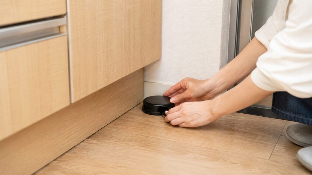 キッチンの隅にベイト剤（毒餌）を設置する、日本人女性の手元