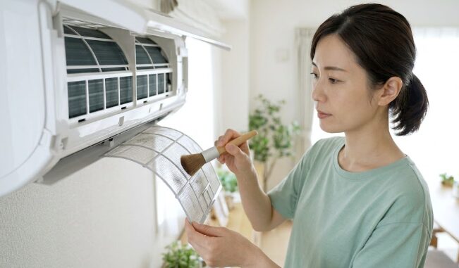 エアコンのフィルターを取り外して丁寧に掃除している日本人の姿。定期的なメンテナンスによる故障予防のイメージ。