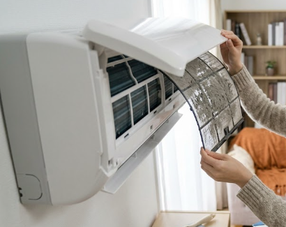 自宅のエアコン室内機の前面パネルを開け、ホコリで目詰まりした汚れたフィルターを取り出している様子。フィルターの目詰まりが暖房効率低下の原因であることを示唆。