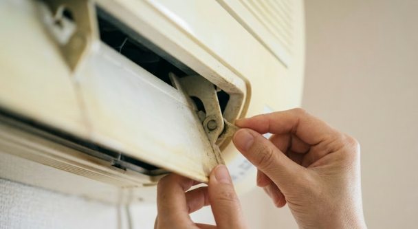 古いエアコンの黄色くなったルーバーの接続部を、破損させないよう慎重に指先で確認する人の手元。